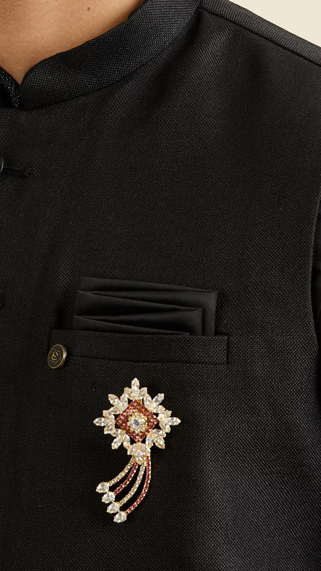 Sparkling gold and rhinestone starburst brooch with hanging tassels pinned onto a black suit lapel.